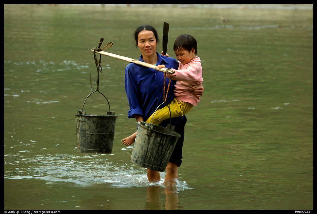 Tay Woman carrying child and water buckets across river. Northeast Vietnam
