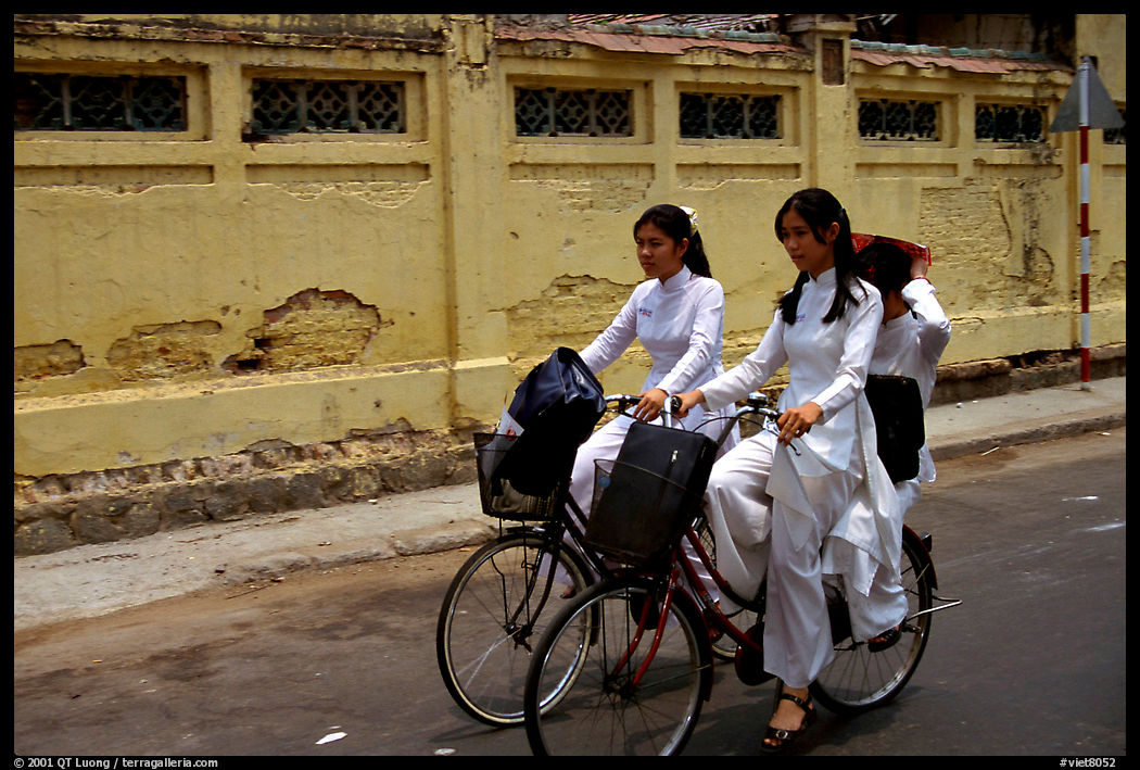 Senior high school girls ride bicycles with impeccable style, wearing elegant Ao Dai uniforms. Ho Chi Minh City, Vietnam