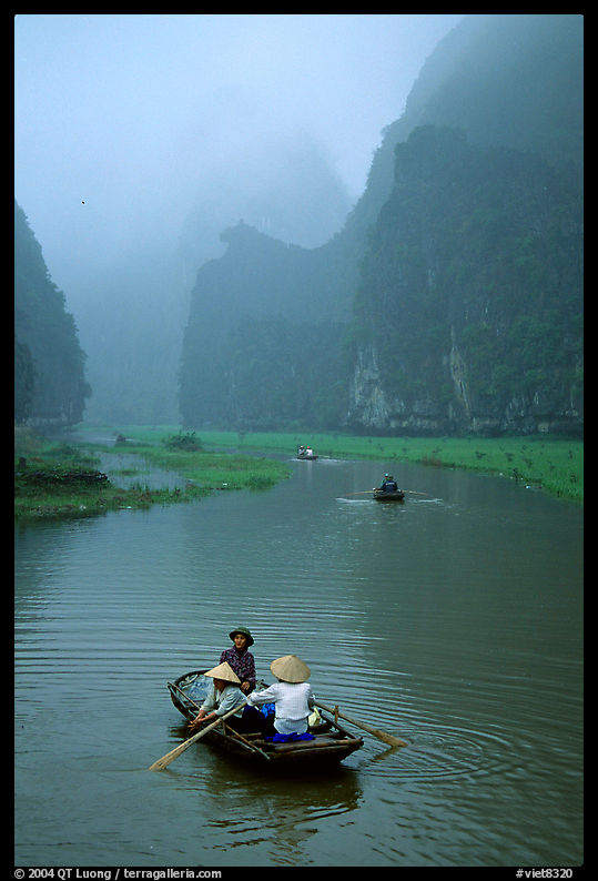 Villagers going by boat to their fields, amongst karstic cliffs in the mist. near Ninh Binh,  Vietnam