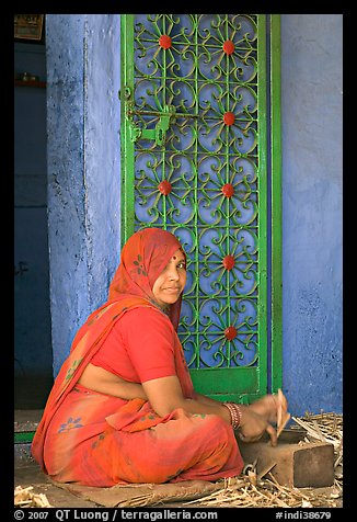 Woman in orange sari sitting next to green door and blue wall. Jodhpur, Rajasthan, India