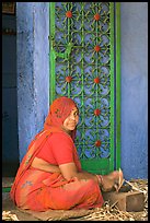 Woman in orange sari sitting next to green door and blue wall. Jodhpur, Rajasthan, India