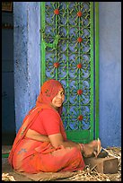 Woman in orange sari sitting next to green door and blue wall. Jodhpur, Rajasthan, India (color)