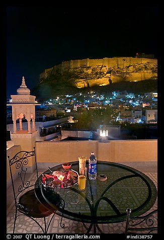 Rooftop restaurant table with food served and view of Mehrangarh Fort by night. Jodhpur, Rajasthan, India (color)