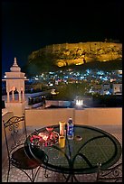 Rooftop restaurant table with food served and view of Mehrangarh Fort by night. Jodhpur, Rajasthan, India