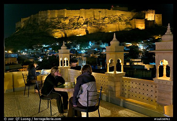 Travelers on rooftop terrace with view of Mehrangarh Fort by night. Jodhpur, Rajasthan, India