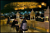 Travelers on rooftop terrace with view of Mehrangarh Fort by night. Jodhpur, Rajasthan, India