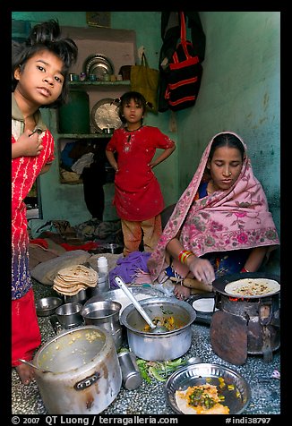 Woman cooking, flanked by two girls. Jodhpur, Rajasthan, India