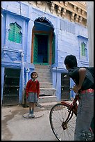 Boy on bicycle looking at girl in front of blue house. Jodhpur, Rajasthan, India