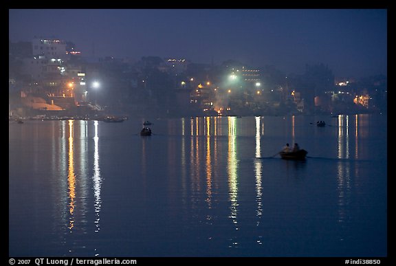 Rowboats and reflected lights on the Ganges River at dusk. Varanasi, Uttar Pradesh, India