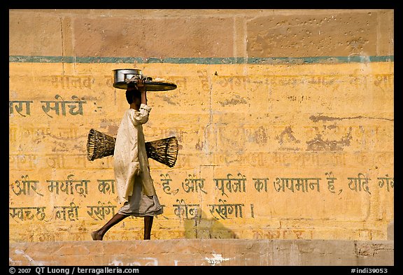 Man carrying a plater in front of wall with inscriptions in Hindi. Varanasi, Uttar Pradesh, India