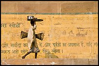 Man carrying a plater in front of wall with inscriptions in Hindi. Varanasi, Uttar Pradesh, India