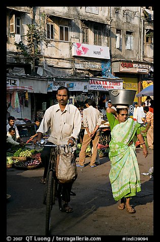 Man riding bike and woman with basket on head, Colaba Market. Mumbai, Maharashtra, India