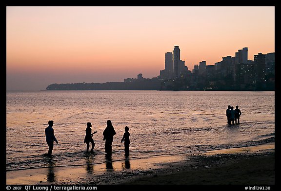 People standing in water at sunset with skyline behind, Chowpatty Beach. Mumbai, Maharashtra, India (color)