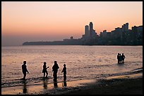 People standing in water at sunset with skyline behind, Chowpatty Beach. Mumbai, Maharashtra, India (color)