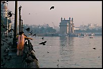 Woman feeding birds, with Gateway of India in background, early morning. Mumbai, Maharashtra, India (color)