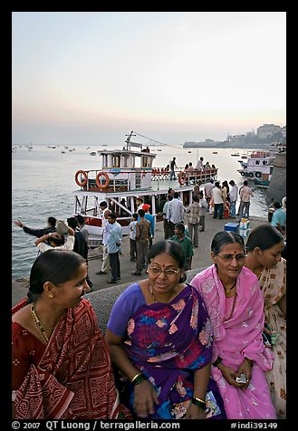 Women sitting on waterfront with boats behind at twilight. Mumbai, Maharashtra, India