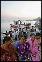 Women sitting on waterfront with boats behind at twilight. Mumbai, Maharashtra, India