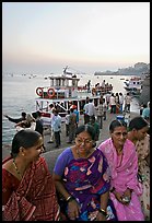 Women sitting on waterfront with boats behind at twilight. Mumbai, Maharashtra, India (color)