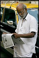 Man reading newspaper next to taxi. Mumbai, Maharashtra, India