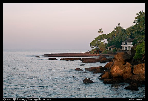 Boulders, beachfront house, and palm trees at sunrise. Goa, India