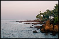 Boulders, beachfront house, and palm trees at sunrise. Goa, India