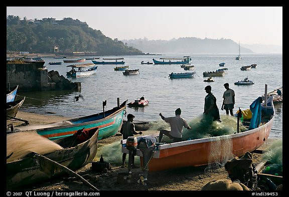 Men repairing net in small fishing boat, early morning, Dona Paula. Goa, India (color)