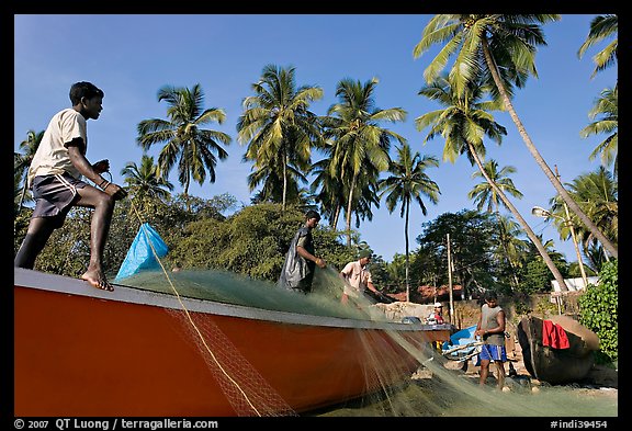 Men mending fishing net with palm trees in background. Goa, India (color)