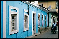 Men on motorbike driving through blue house, Panjim. Goa, India