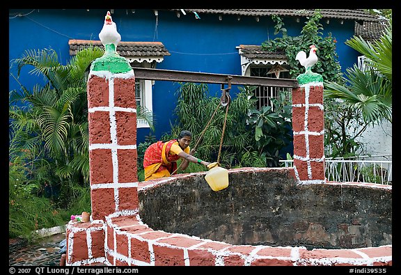 Woman retrieving water from well with blue house behind, Panjim. Goa, India (color)