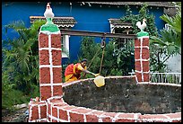 Woman retrieving water from well with blue house behind, Panjim. Goa, India (color)