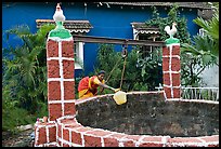 Woman retrieving water from well with blue house behind, Panjim. Goa, India