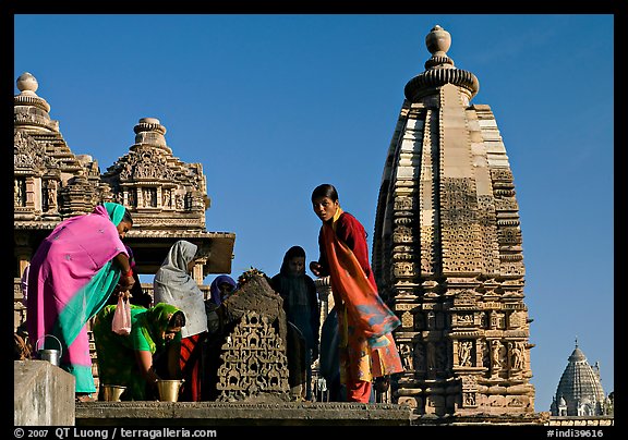 Women worshipping image with of Vahara and Lakshmana temples behind. Khajuraho, Madhya Pradesh, India