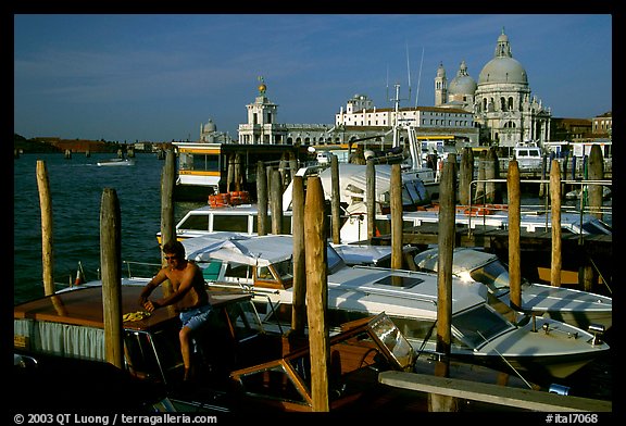 Water taxi driver cleaning out his boat in the morning, Santa Maria della Salute in the background. Venice, Veneto, Italy (color)