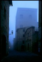 Street and medieval tower at dawn in the fog. San Gimignano, Tuscany, Italy (color)