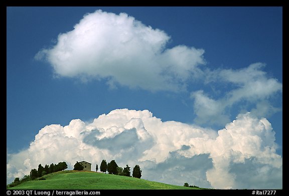 Fluffy clouds above ridge with cypress trees and house. Tuscany, Italy (color)