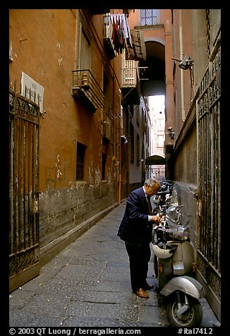 Man locking his motorbike in a side street. Naples, Campania, Italy (color)