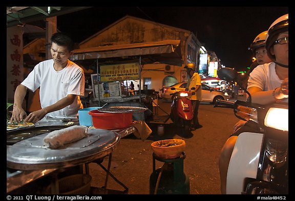 Man preparing food as people wait on motorbike. George Town, Penang, Malaysia