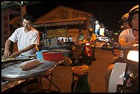 Man preparing food as people wait on motorbike. George Town, Penang, Malaysia ( color)