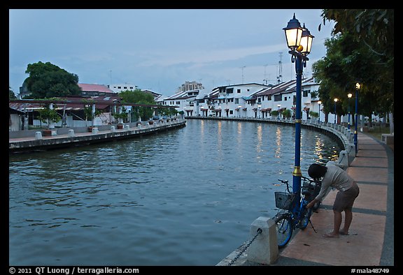 Woman locking bicyle on quay of Melaka River. Malacca City, Malaysia (color)