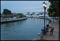 Woman locking bicyle on quay of Melaka River. Malacca City, Malaysia