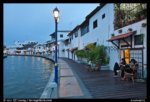 Women relaxing in front of riverside house, dusk. Malacca City, Malaysia