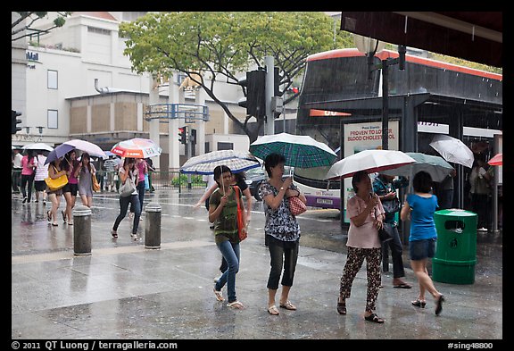 Women cross street of shopping area during shower. Singapore (color)