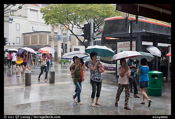 Women cross street of shopping area during shower. Singapore