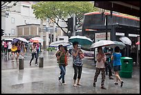 Women cross street of shopping area during shower. Singapore