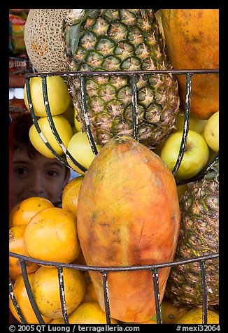 Boy peers from behind fruits offered at a juice stand, Tlaquepaque. Jalisco, Mexico (color)
