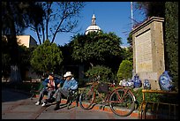 Men sitting in garden, with cathedral dome and ceramic monument, Tlaquepaque. Jalisco, Mexico (color)