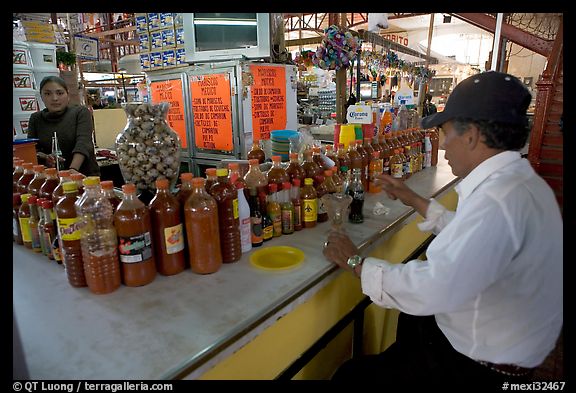 Man sitting at a booth offering a large variety of bottled chili. Guanajuato, Mexico (color)