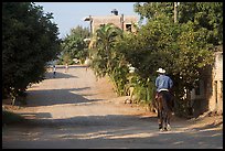 Man on horse going down a village street. Mexico