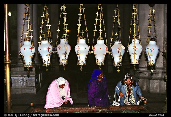 Women worshiping beneath hanging lamps inside the Church of the Holy Sepulchre. Jerusalem, Israel