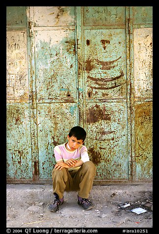 Young boy sitting in front of a closed store, Hebron. West Bank, Occupied Territories (Israel) (color)